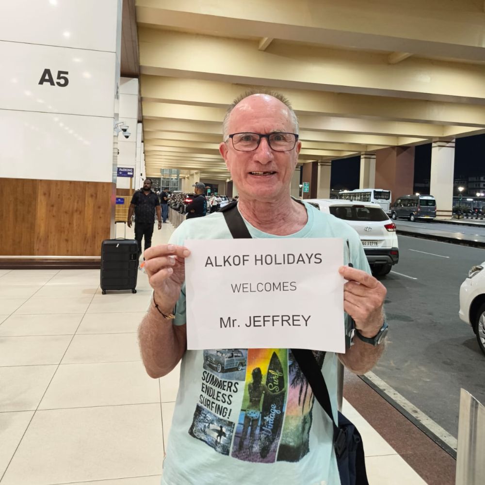 Happy traveller at airport arrivals holding Alkof Holidays welcome board
